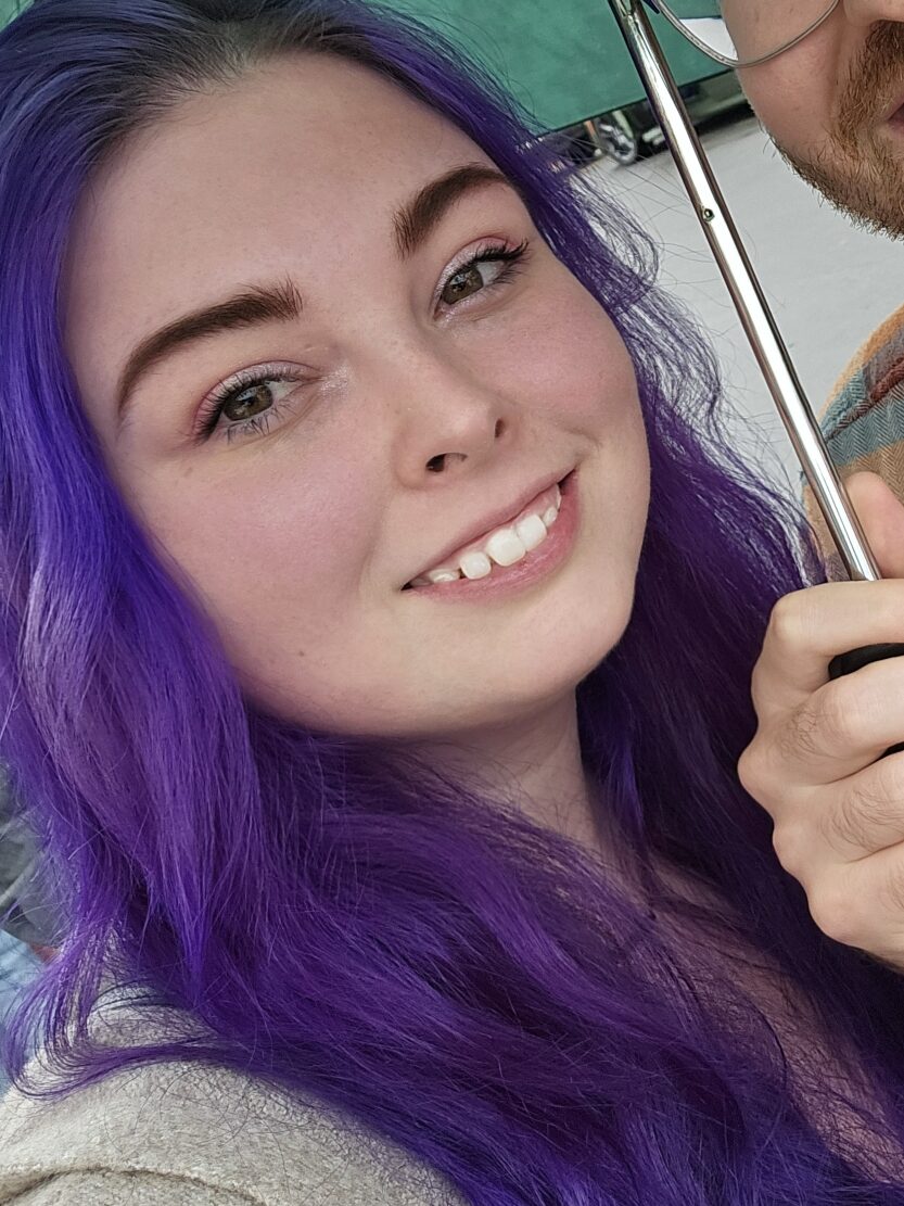 Image of Mackenzie with vibrant purple hair and smiling.